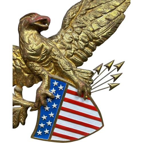 213 - A GILT PAINTED AMERICAN EAGLE WALL HANGING, above a United States Stars and Stripes with five arrows... 