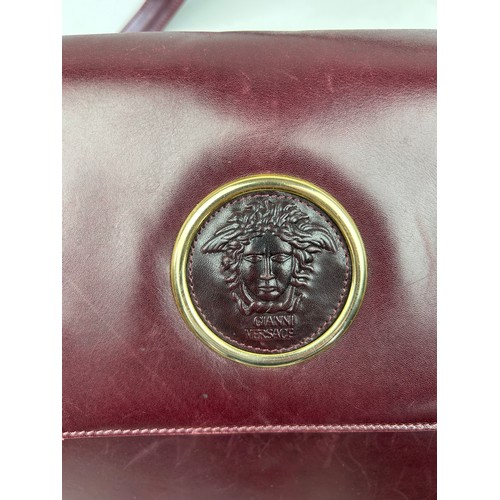 28 - A VINTAGE VERSACE BURGUNDY LEATHER FLAP BAG, with central Medusa head emblem and leather strap.

26c... 