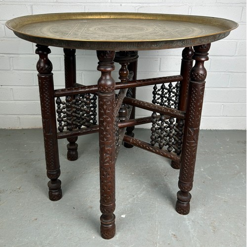 478 - A 19TH CENTURY MOROCCAN FOLDING TABLE, with a brass tray top, 64cm diameter x 57.5cm h 

Used condit... 