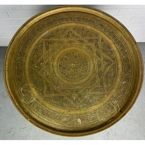 478 - A 19TH CENTURY MOROCCAN FOLDING TABLE, with a brass tray top, 64cm diameter x 57.5cm h 

Used condit... 