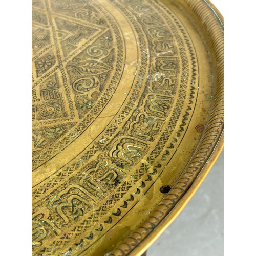 478 - A 19TH CENTURY MOROCCAN FOLDING TABLE, with a brass tray top, 64cm diameter x 57.5cm h 

Used condit... 