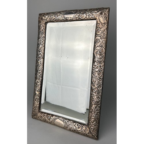 154 - A FOREIGN REPOUSSE SILVER PICTURE FRAME MIRROR DECORATED WITH FLOWERS,

36cm x 23cm