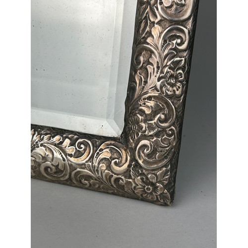 154 - A FOREIGN REPOUSSE SILVER PICTURE FRAME MIRROR DECORATED WITH FLOWERS,

36cm x 23cm