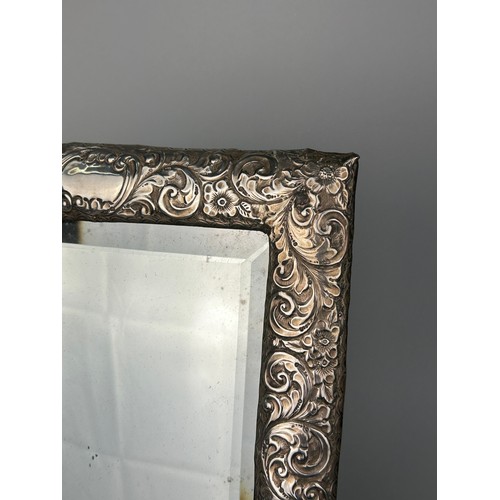 154 - A FOREIGN REPOUSSE SILVER PICTURE FRAME MIRROR DECORATED WITH FLOWERS,

36cm x 23cm