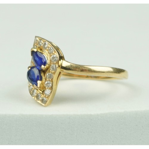 323 - A GOLD RING 18CT GOLD SET WITH TWO CENTRAL PEAR DROP CUT SAPPHIRES, SURROUNDED BY SMALL DIAMONDS,