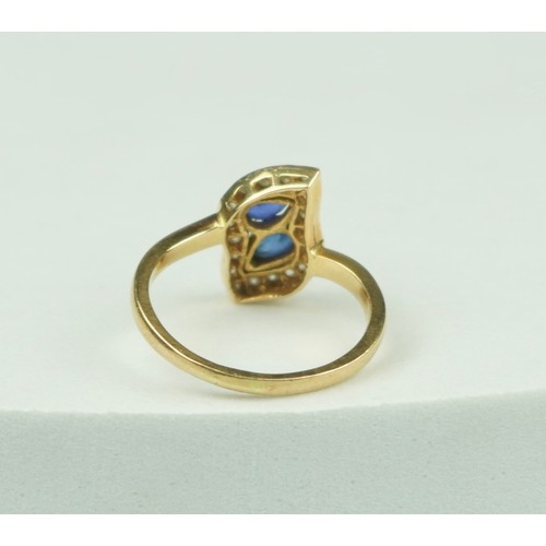 323 - A GOLD RING 18CT GOLD SET WITH TWO CENTRAL PEAR DROP CUT SAPPHIRES, SURROUNDED BY SMALL DIAMONDS,