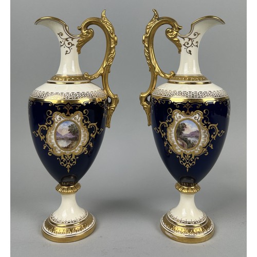 667 - A PAIR OF COALPORT PORCELAIN EWERS BLUE GROUND WITH GILT AND CENTRAL PAINTED PANELS DEPICTING LANDSC... 