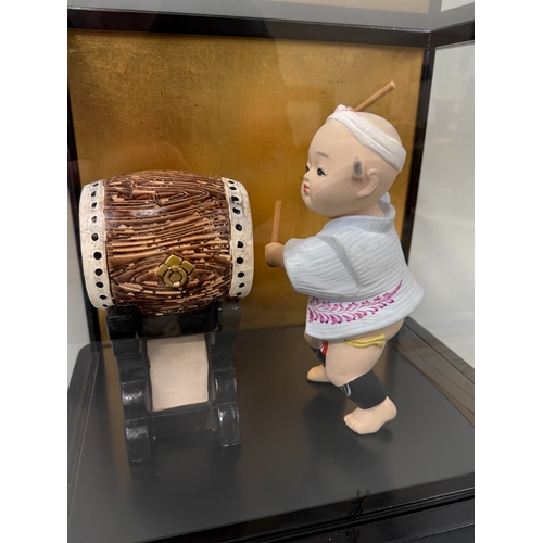 1014 - A JAPANESE CERAMIC MODEL OF A CHILD HITTING A DRUM, IN GLASS CASE
38cm x 34cm x 28cm