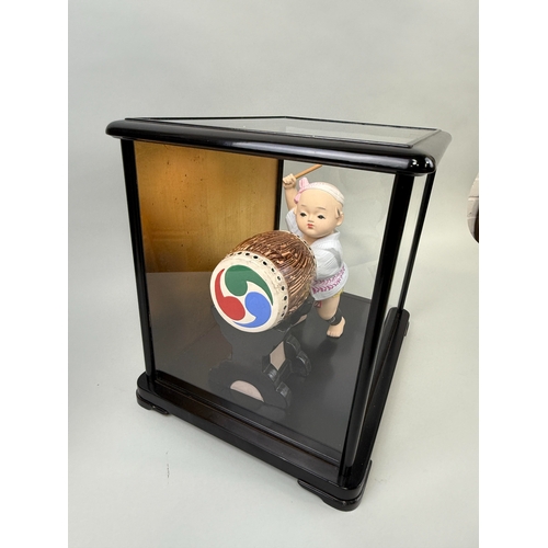 1014 - A JAPANESE CERAMIC MODEL OF A CHILD HITTING A DRUM, IN GLASS CASE
38cm x 34cm x 28cm