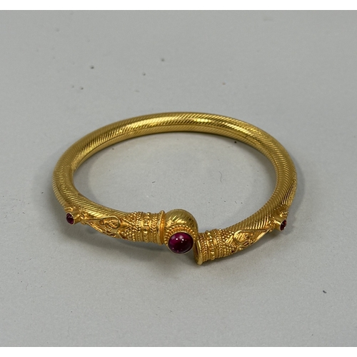 174 - AN INDIAN GOLD TONE BANGLE WITH RED STONES
 