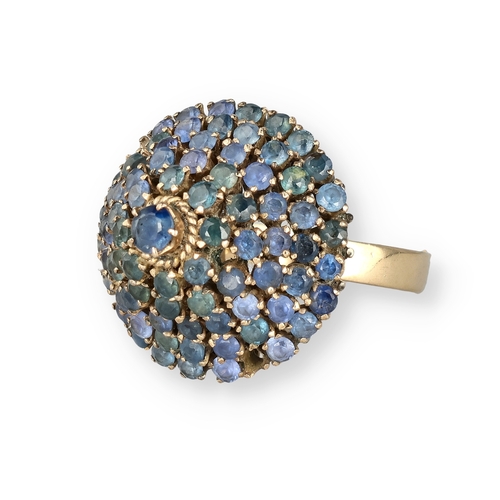 19 - AN 18 CARAT GOLD BOMBÉ RING, CLAW SET WITH FIVE ROWS OF SAPPHIRES
The central stone in a ropetwist s... 