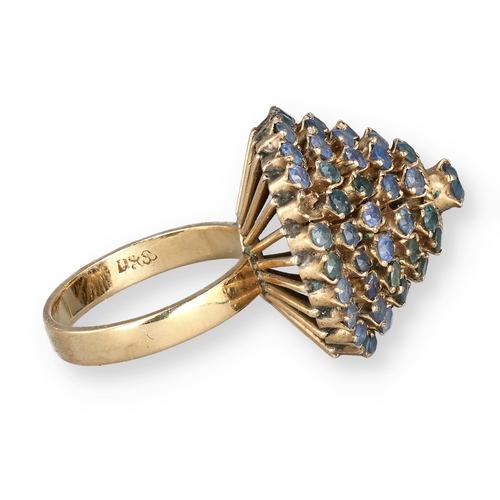 19 - AN 18 CARAT GOLD BOMBÉ RING, CLAW SET WITH FIVE ROWS OF SAPPHIRES
The central stone in a ropetwist s... 