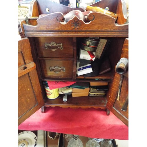 202 - A vintage smokers cabinet and contents having carved double doors enclosing inner compartment and pi... 