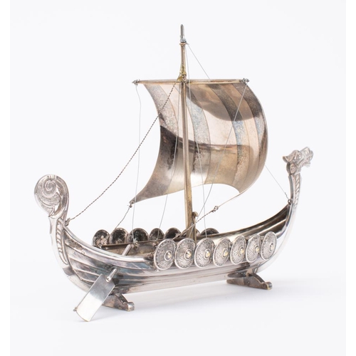 58 - A continental white metal model of a Viking longship: set sail over carved bow and stern  uprights w... 