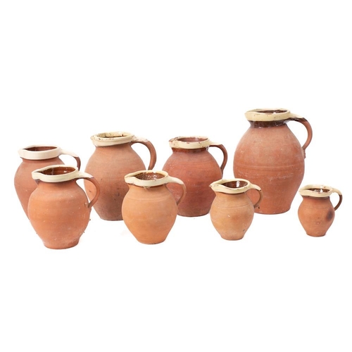 473 - A collection of eight graduated terracotta jugs: with cream slip glazed rims.