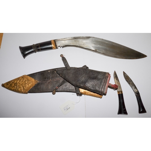 165 - A Malayan Kukri: with 34cm single edged blade, horn grip, with two smaller knives contained in a lea... 