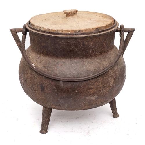 82 - A bronze twin-handled cauldron: of bag shape with iron swing handle and tripod feet, having stone co... 