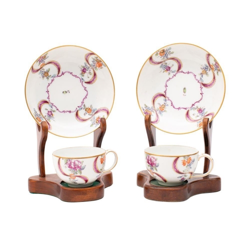 111 - A pair of Zurich teacups and saucers, each painted with floral sprays amongst puce ribbons around a ... 