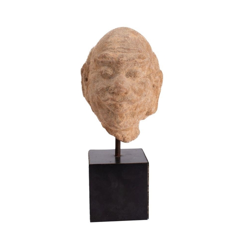 561 - An Indian carved sandstone head of a moustachioed man with shaved head, furrowed forehead, bushy eye... 