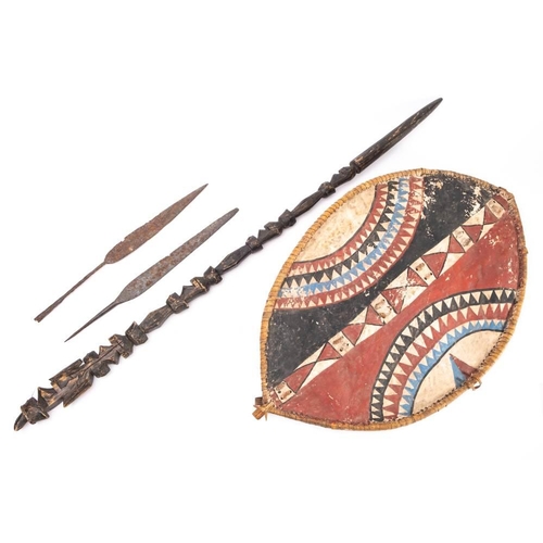 653 - Two African?  steel spear heads of flat leaf form, together with a painted hide shield and a  relief... 
