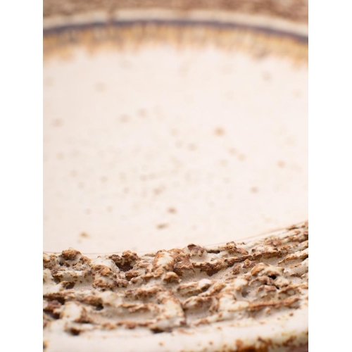 131 - A grogged stoneware charger, with deeply textured border under ivory glazes and a flown russet band,... 