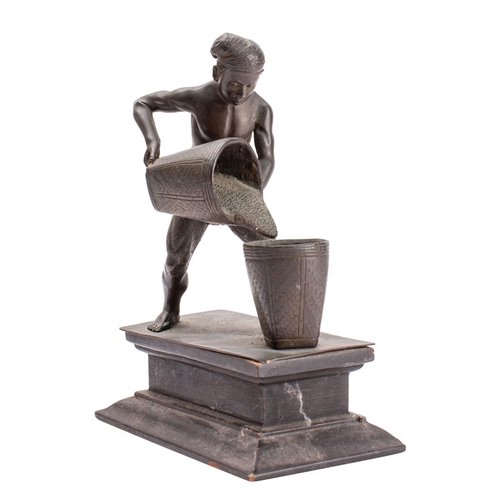 386 - A Burmese figural bronze in the form of a worker wearing a loincloth pouring grain from one basket i... 