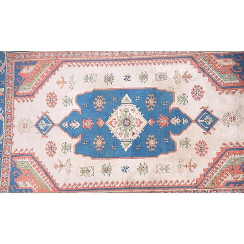 1082 - A Turkish carpet, the camel field with a central pastel blue geometric pole medallion with lozenge c... 