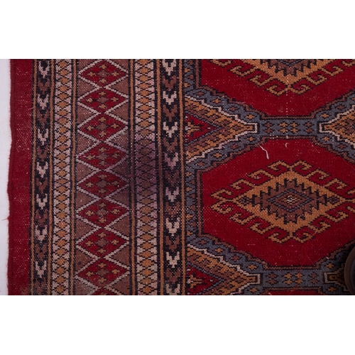 1086 - A Pakistan rug of Turkoman design, the red octagonal panelled field with repeated hooked lozenge med... 