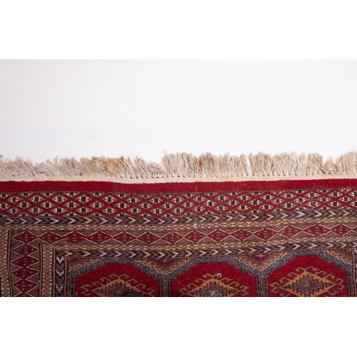 1086 - A Pakistan rug of Turkoman design, the red octagonal panelled field with repeated hooked lozenge med... 