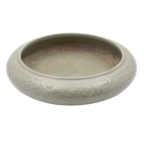 74 - A Chinese celadon bowl of compressed form, decorated in relief with dragons amongst scrolling tendri... 