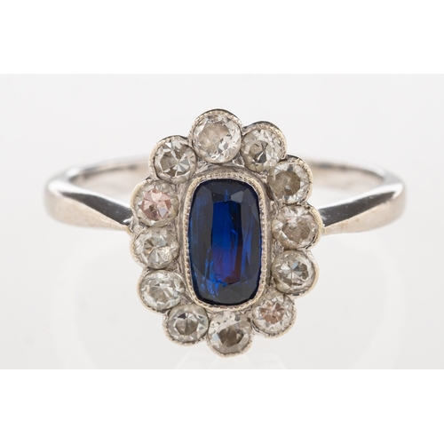 1107 - A cluster ring, set to the centre with an elongated oval synthetic sapphire with a surround of singl... 