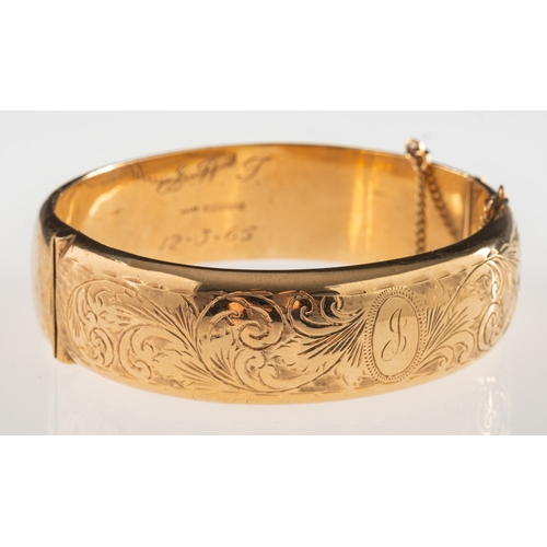 798 - A 9ct gold hinged bangle, with foliate engraving to front panel, safety chain, UK hallmark, inner di... 