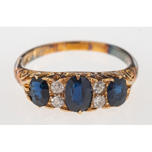 704 - A sapphire and diamond ring, a 'gypsy' style scroll carved ring set with three oval-cut sapphires, i... 