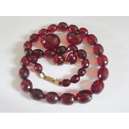 525 - A Faux Cherry Amber Faceted and Graduated Bead Necklace, 76cm largest bead 30x25mm 174g with matchin... 