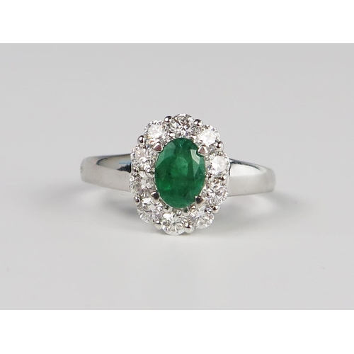 302b - A 14K White Gold, Emerald and Diamond Oval Cluster Ring, the central 7 x 5 mm stone surrounded by 10... 