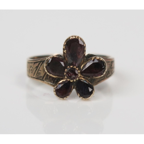 303 - Antique Garnet Flower Head Ring in an unmarked yellow metal setting with chased soldiers shoulders, ... 