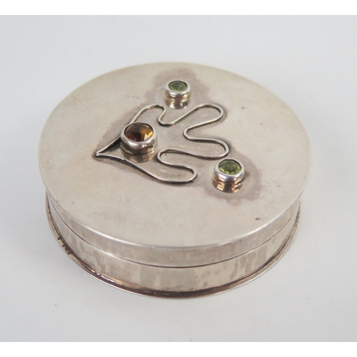 657 - A Contemporary silver Box, of circular form, the pull off lid set with brown and green gems and leaf... 