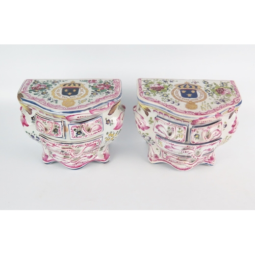 1245 - A pair of faience commodes of bombe-shaped outline, the tops bearing armorials enclosed by floral sp... 