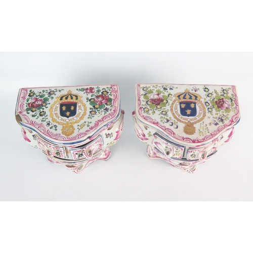 1245 - A pair of faience commodes of bombe-shaped outline, the tops bearing armorials enclosed by floral sp... 