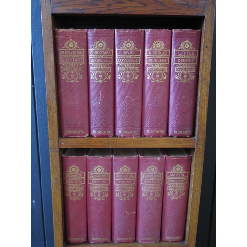 1312 - A 1920's oak bookcase containing fifteen volumes of the works of Charles Dickens. 31cm wide