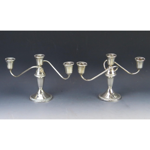 553 - A pair of sterling silver twin branch candelabra stamped Sterling, with urn-shaped sconces on swept ... 