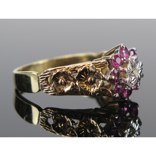 62 - A 9ct Gold Ruby and Diamond Cluster Ring with pierced floral decorated shoulders, c. 12mm wide head,... 