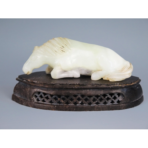 1436 - A Chinese carved jade figure of a recumbent horse, 9.5cm long, on a polished hardstone stand.