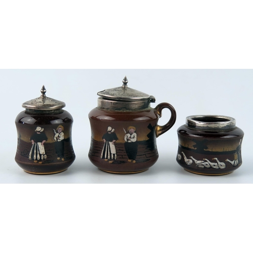 1334 - Taylor Tunnicliffe & Co., a pottery and silver mounted three-piece condiment set, with painted Dutch... 