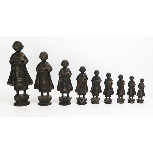 1151 - A collection of nine graduated Burmese bronze monks in traditional robes each carrying a bowl, heigh... 