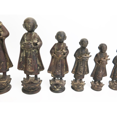 1151 - A collection of nine graduated Burmese bronze monks in traditional robes each carrying a bowl, heigh... 