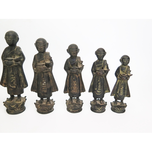 1151 - A collection of nine graduated Burmese bronze monks in traditional robes each carrying a bowl, heigh... 