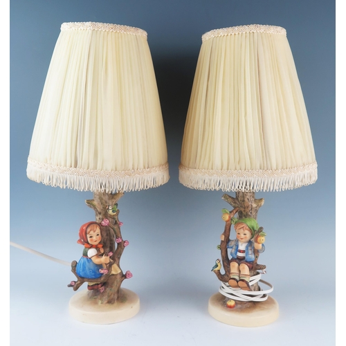 1022 - A pair of Goebel porcelain table lamps, decorated with children seated in bowers, impressed M J Humm... 