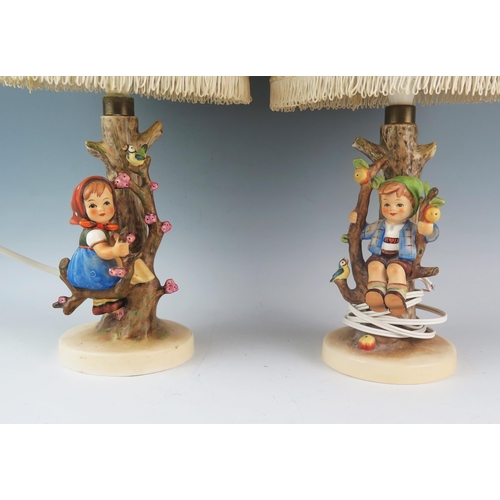 1022 - A pair of Goebel porcelain table lamps, decorated with children seated in bowers, impressed M J Humm... 