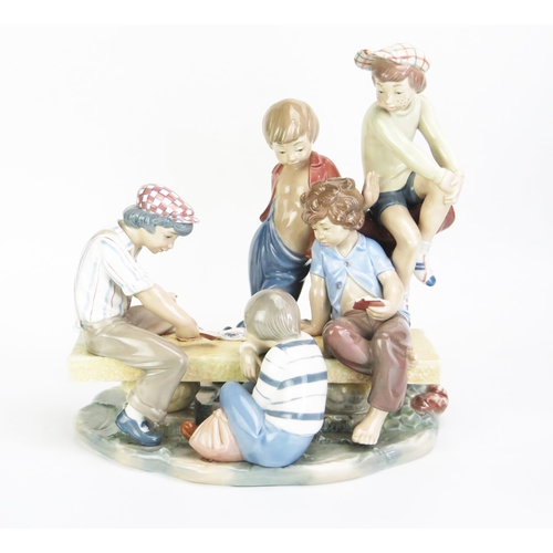 1045 - A large Nao porcelain figure group of street urchins playing cards on a bench, 32cm high, 30cm wide.